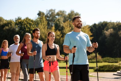 Photo of Group of people practicing Nordic walking with poles in park on sunny day