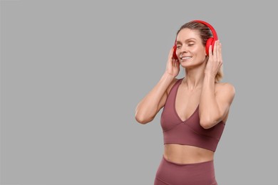 Sportswoman with headphones on grey background, space for text