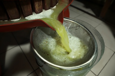 Grape juice pouring from wooden wine press into bucket indoors, closeup