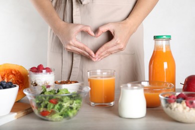 Photo of Woman making heart near table with food, closeup. Balanced nutrition for healthy digestive system