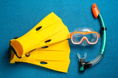 Photo of Pair of yellow flippers and mask on blue fabric, flat lay