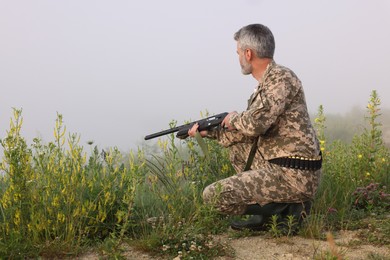 Man wearing camouflage with hunting rifle outdoors. Space for text