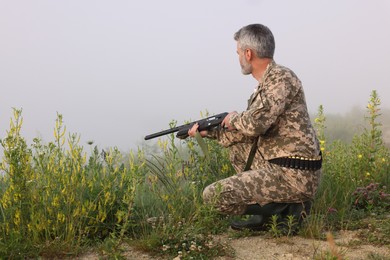 Photo of Man wearing camouflage with hunting rifle outdoors. Space for text