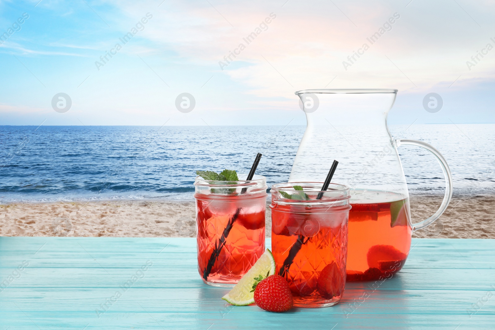 Image of Tasty refreshing drink on wooden table against sandy beach