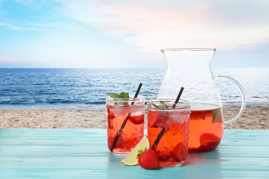 Image of Tasty refreshing drink on wooden table against sandy beach