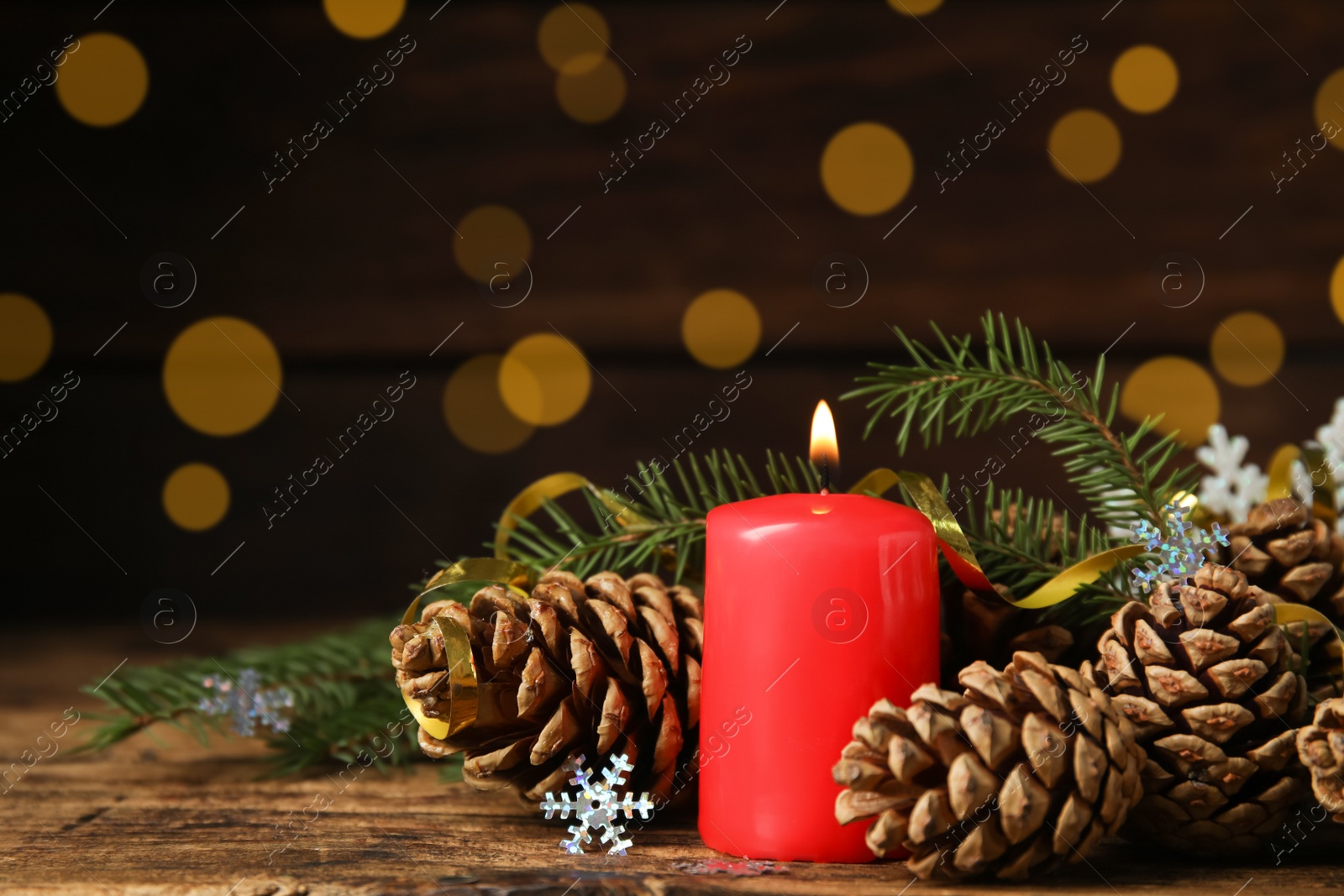 Photo of Burning candle, pine cones and fir tree branches on wooden table against blurred festive lights, space for text. Christmas eve