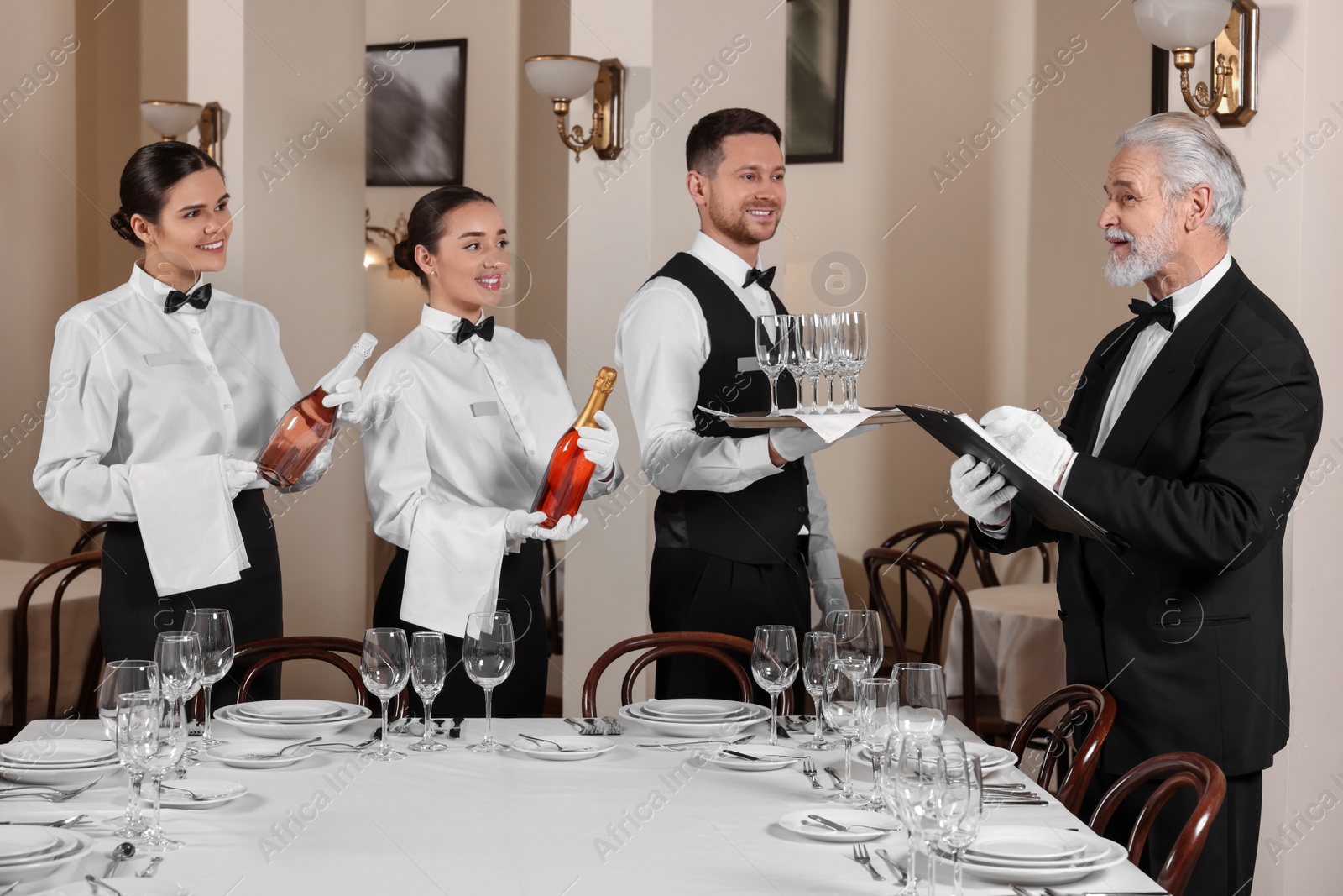 Photo of Senior man wearing formal suit teaching trainees in restaurant. Professional butler courses