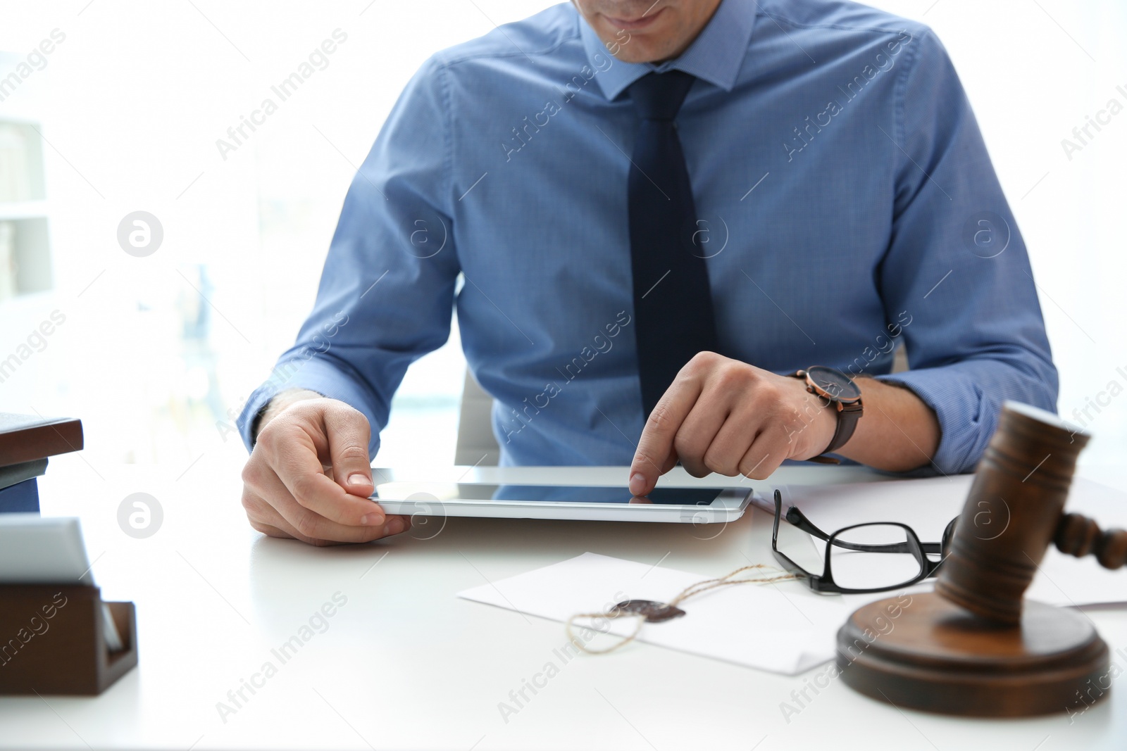 Photo of Notary working with tablet and judge gavel on table, closeup. Law and justice concept