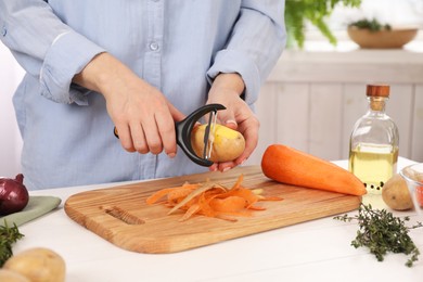 Photo of Woman peeling fresh potato at white wooden table indoors, closeup