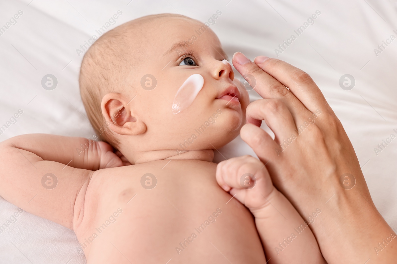 Photo of Woman applying cream onto baby`s face on bed, closeup