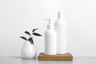 Photo of Bottles with different cosmetic products and green leaves in vase on light grey table against white background