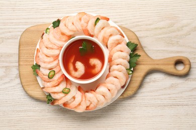 Photo of Tasty boiled shrimps with cocktail sauce, chili and parsley on light wooden table, top view