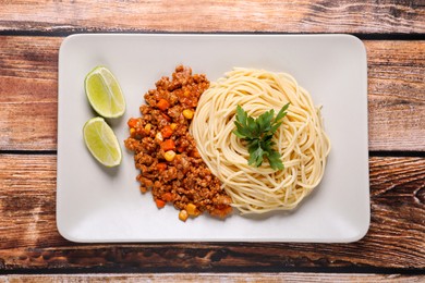 Tasty dish with fried minced meat, spaghetti, carrot and corn served on wooden table, top view