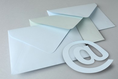 Image of White paper envelopes and at sign on light grey background, closeup. Email service