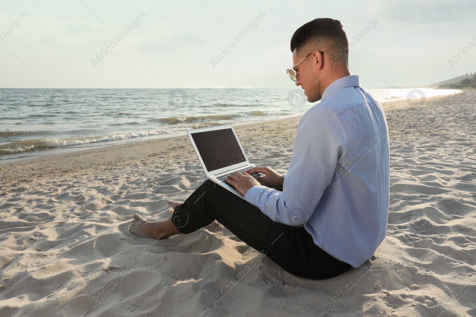 Photo of Businessman working with laptop on beach. Business trip