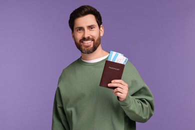 Smiling man with passport and tickets on purple background