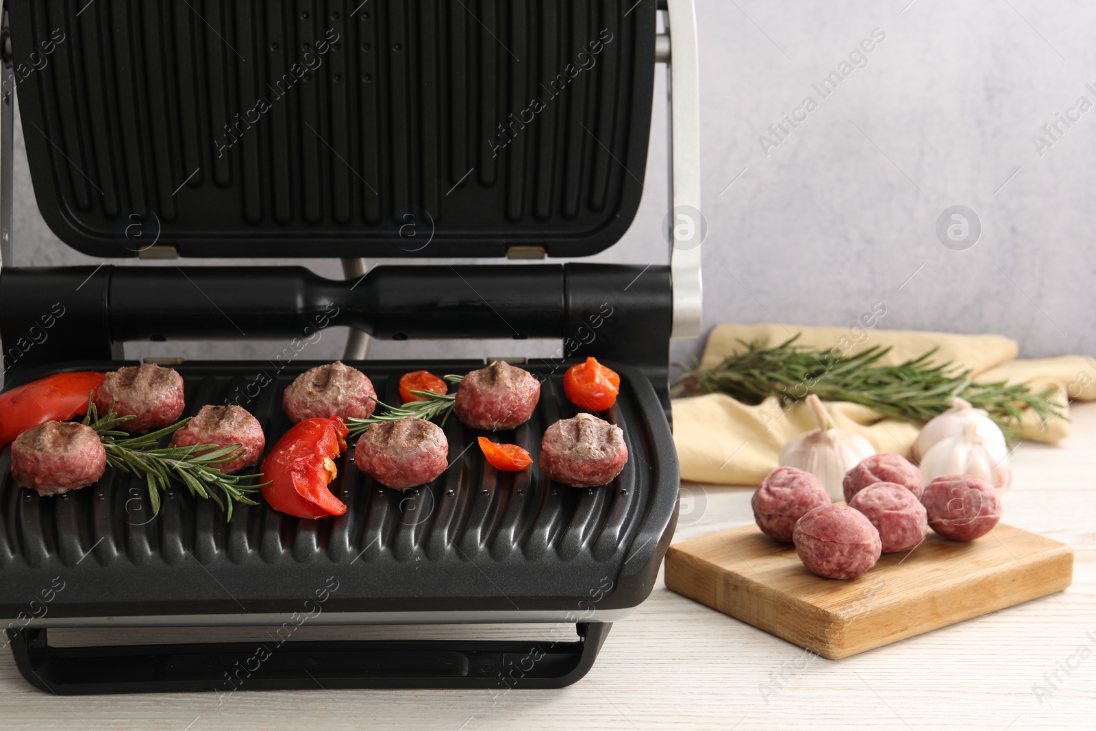 Photo of Electric grill with vegetables, meat balls and rosemary on wooden table