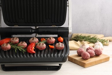 Photo of Electric grill with vegetables, meat balls and rosemary on wooden table