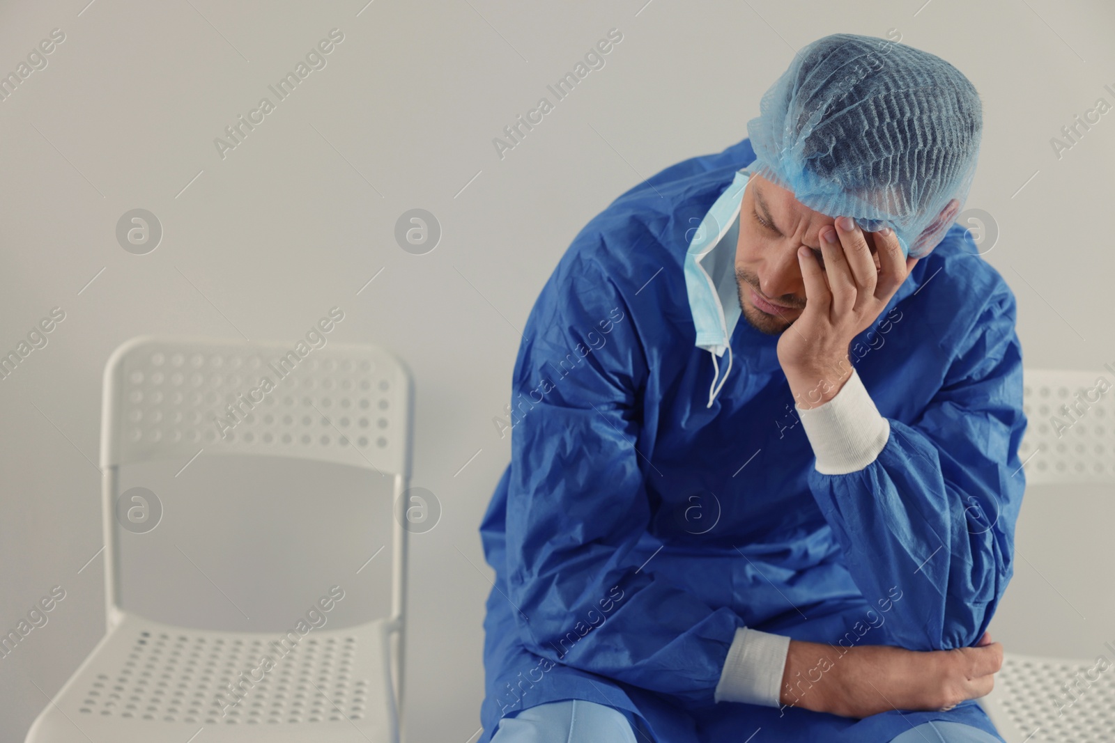 Photo of Exhausted doctor sitting on chair near grey wall, space for text