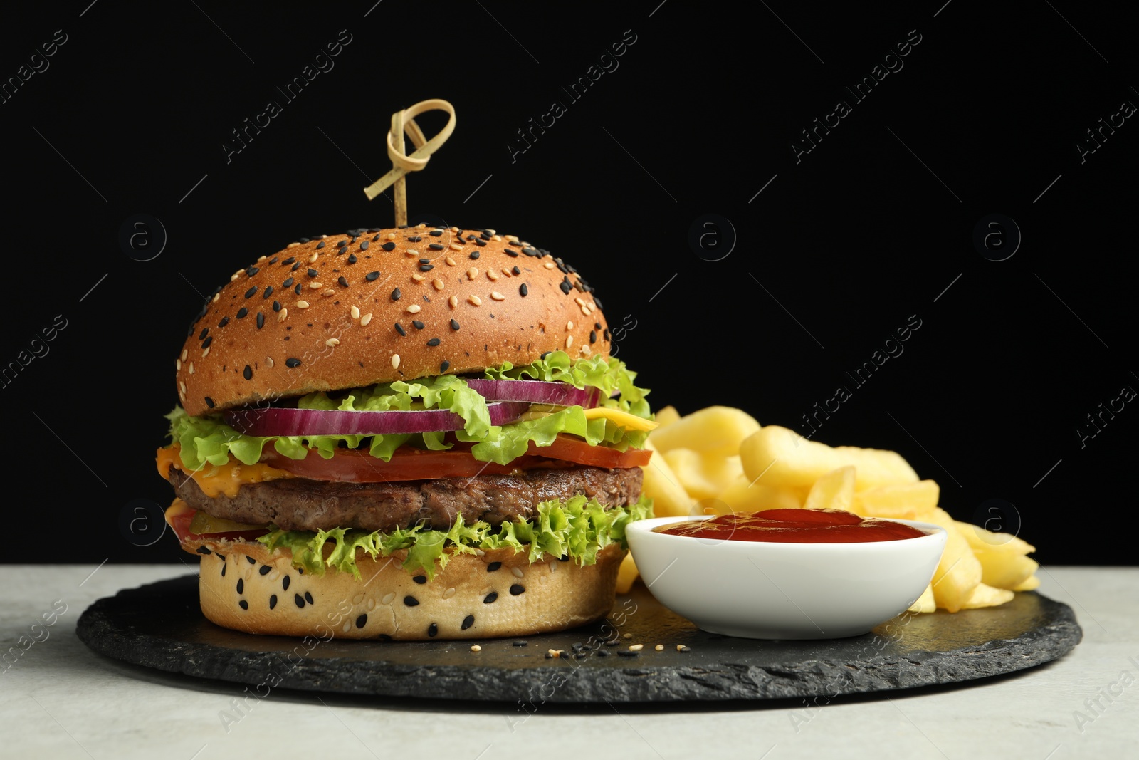 Burger with delicious patty, french fries and sauce on gray table against black background Photo of Burger with delicious patty, french fries and sauce on gray table against black background