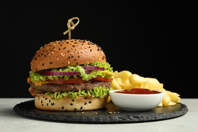 Photo of Burger with delicious patty, french fries and sauce on gray table against black background