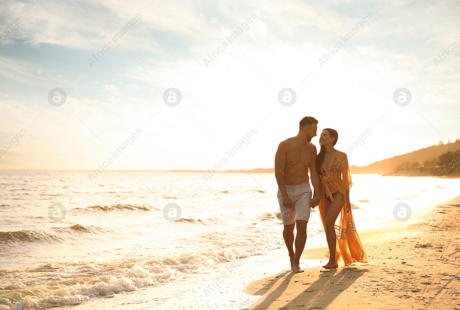 Photo of Happy young couple walking together on beach at sunset