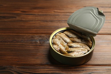 Photo of Open tin can of sprats on wooden table. Space for text
