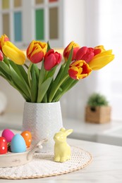 Easter decorations. Bouquet of tulips, painted eggs and bunny figure on table indoors, closeup