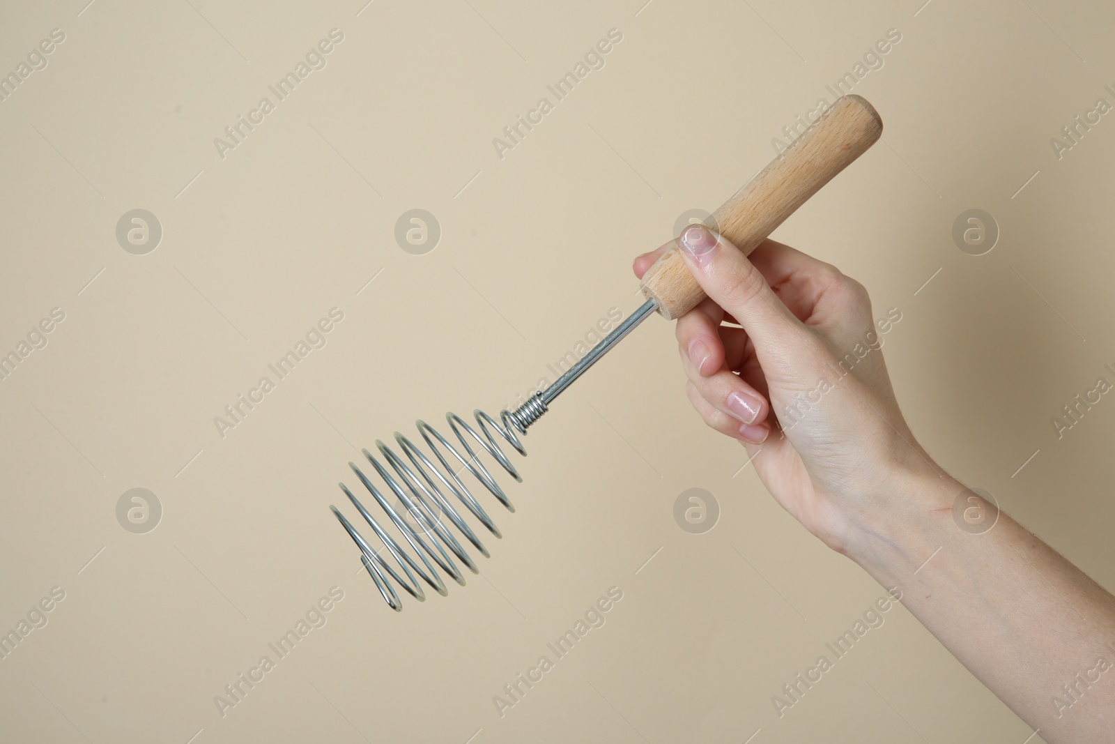 Photo of Woman holding metal whisk on beige background, closeup