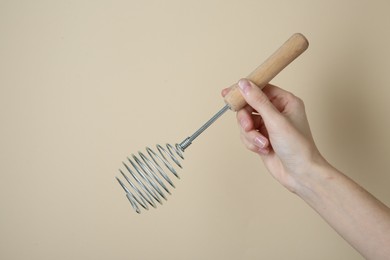 Woman holding metal whisk on beige background, closeup