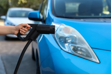 Photo of Woman holding power supply cable at electric vehicle charging station, closeup