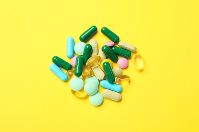 Photo of Different vitamin pills on yellow background, top view