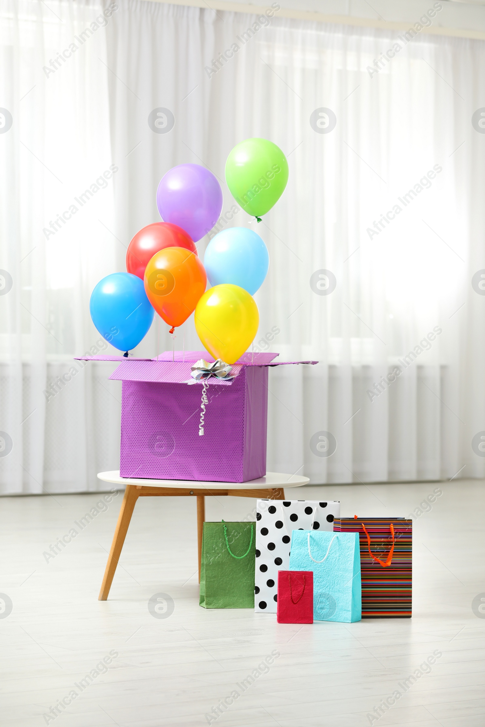 Photo of Gift box with bright air balloons and gift bags indoors