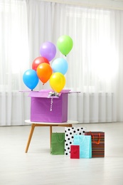 Photo of Gift box with bright air balloons and gift bags indoors