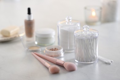 Photo of Cotton buds and pads in transparent holders near makeup brushes on table indoors