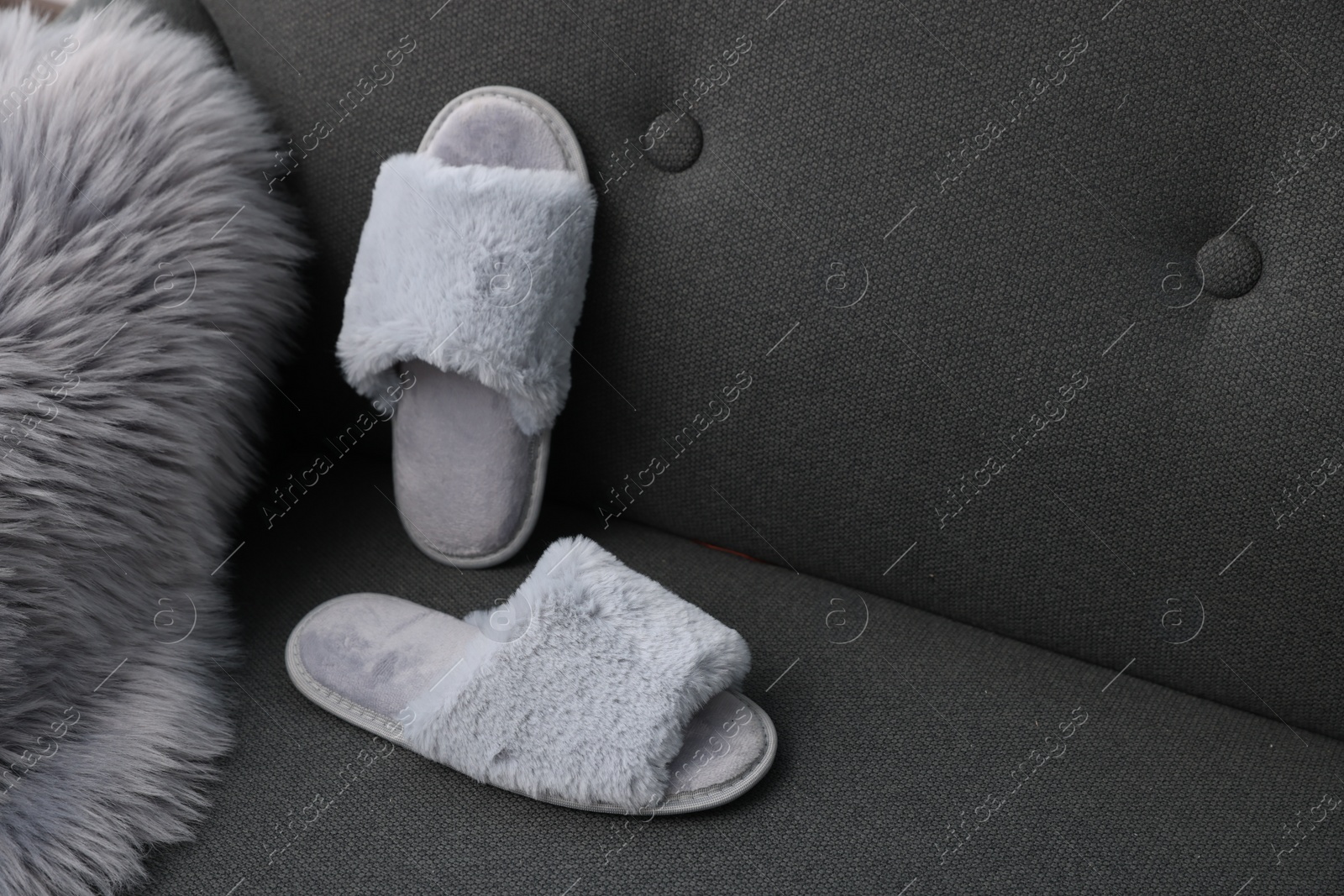 Photo of Soft grey slippers and faux fur on sofa, space for text