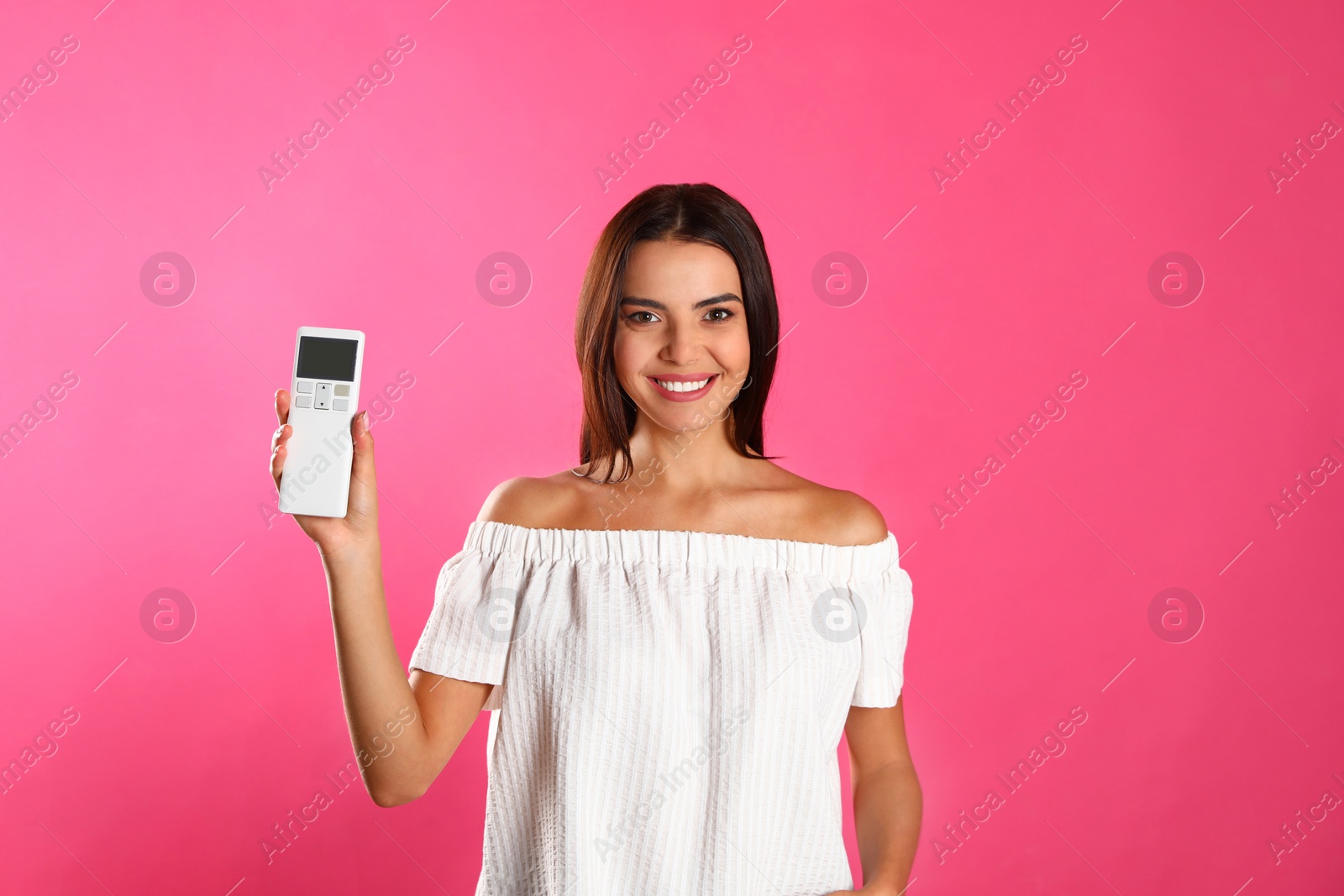 Photo of Young woman with air conditioner remote on pink background