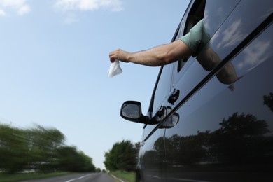 Photo of Driver throwing away wet wipe from car window, low angle view. Garbage on road