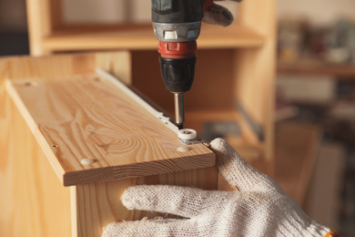 Photo of Professional carpenter twisting screw into wooden drawer in workshop, closeup