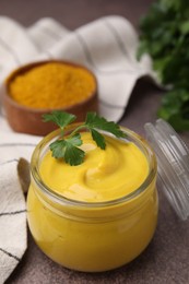 Photo of Jar with tasty curry sauce, powder and parsley on brown table