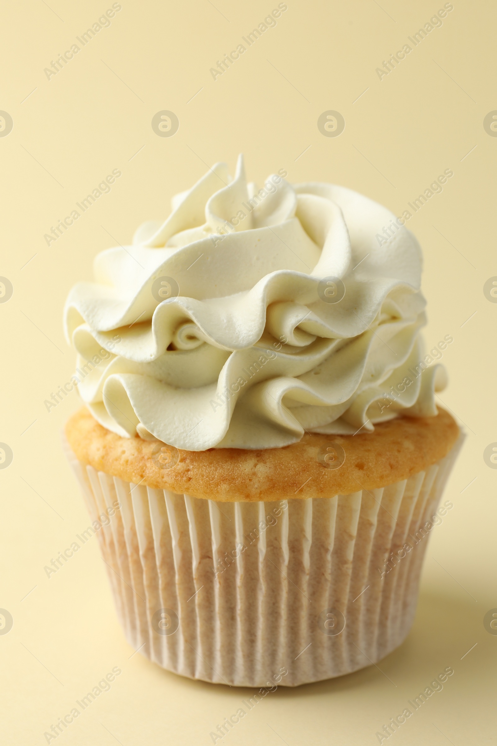 Photo of Tasty vanilla cupcake with cream on pale yellow background, closeup