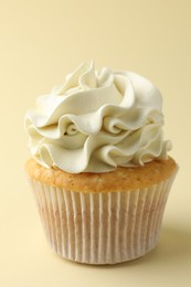 Tasty vanilla cupcake with cream on pale yellow background, closeup