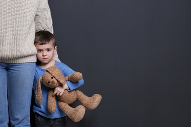 Sad little boy with toy hugging his mother on black background, space for text