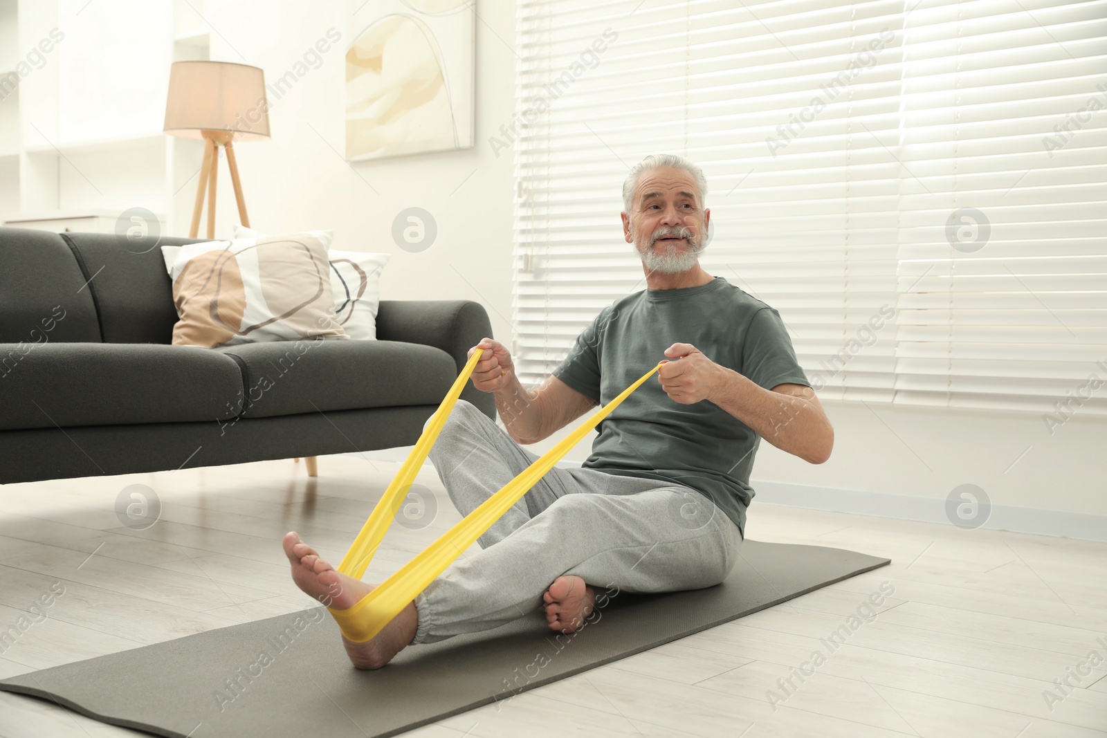 Photo of Senior man doing exercise with fitness elastic band on mat at home