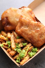 Photo of Tasty fish, chips and peas in paper box on grey table, above view