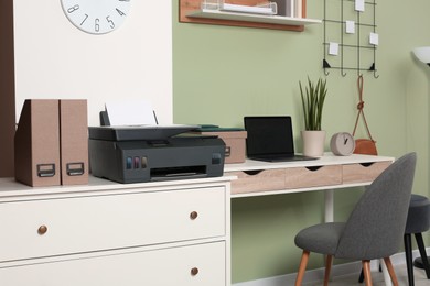 Modern printer with paper on white chest of drawers near stylish workplace indoors