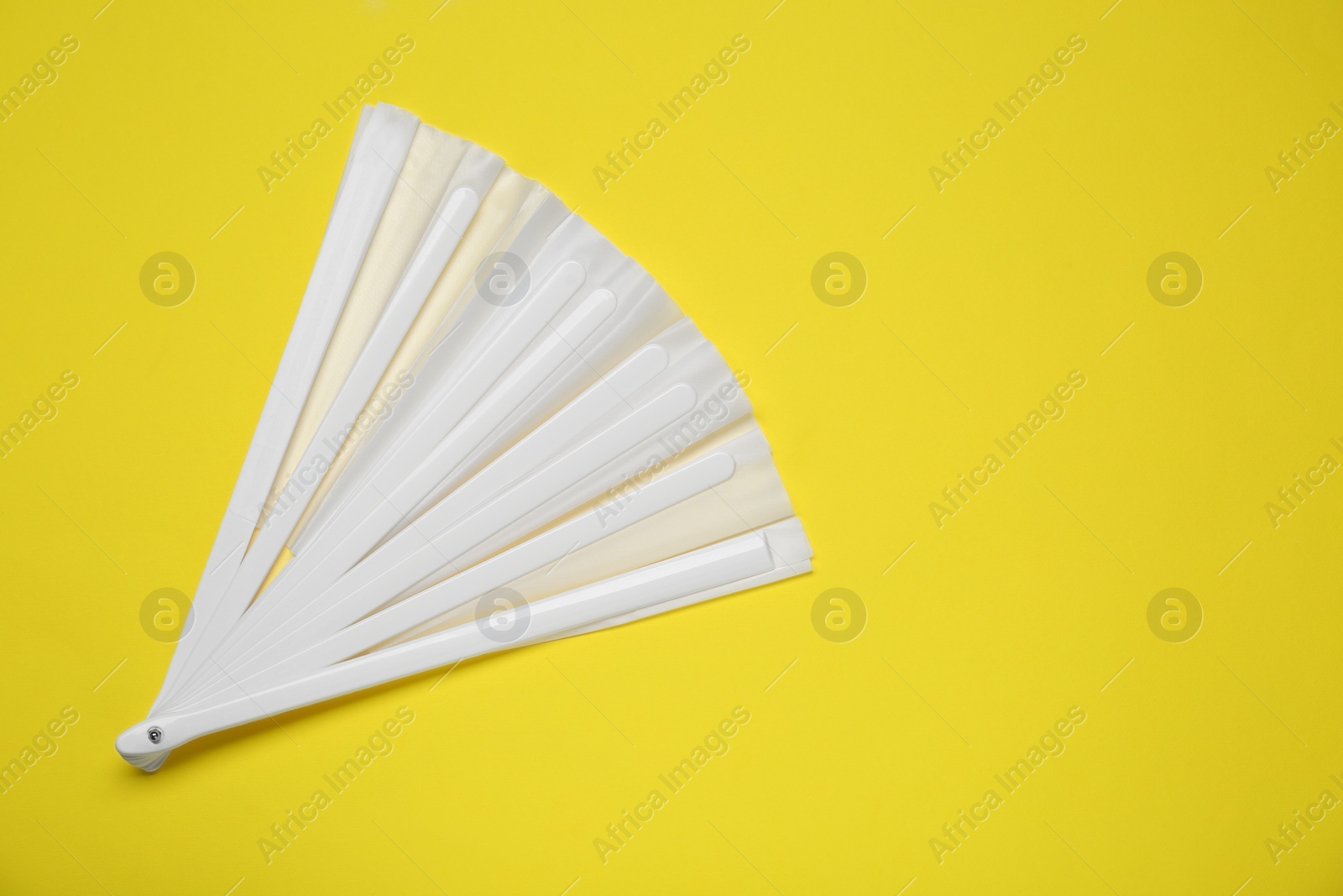 Photo of White hand fan on yellow background, top view. Space for text