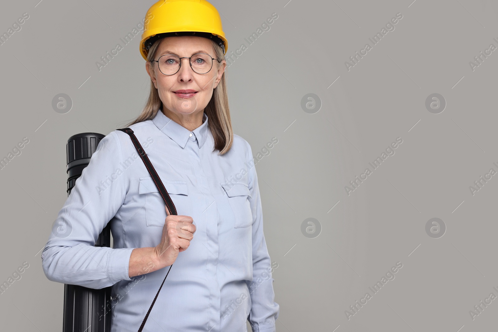 Photo of Architect in hard hat with tube on grey background, space for text