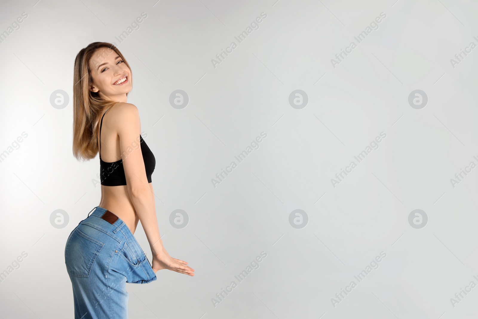 Photo of Slim woman in oversized jeans on light background, space for text. Perfect body