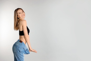 Photo of Slim woman in oversized jeans on light background, space for text. Perfect body